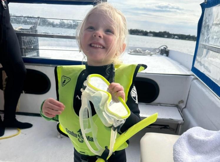 A little girl on a boat in snorkeling gear smiling.